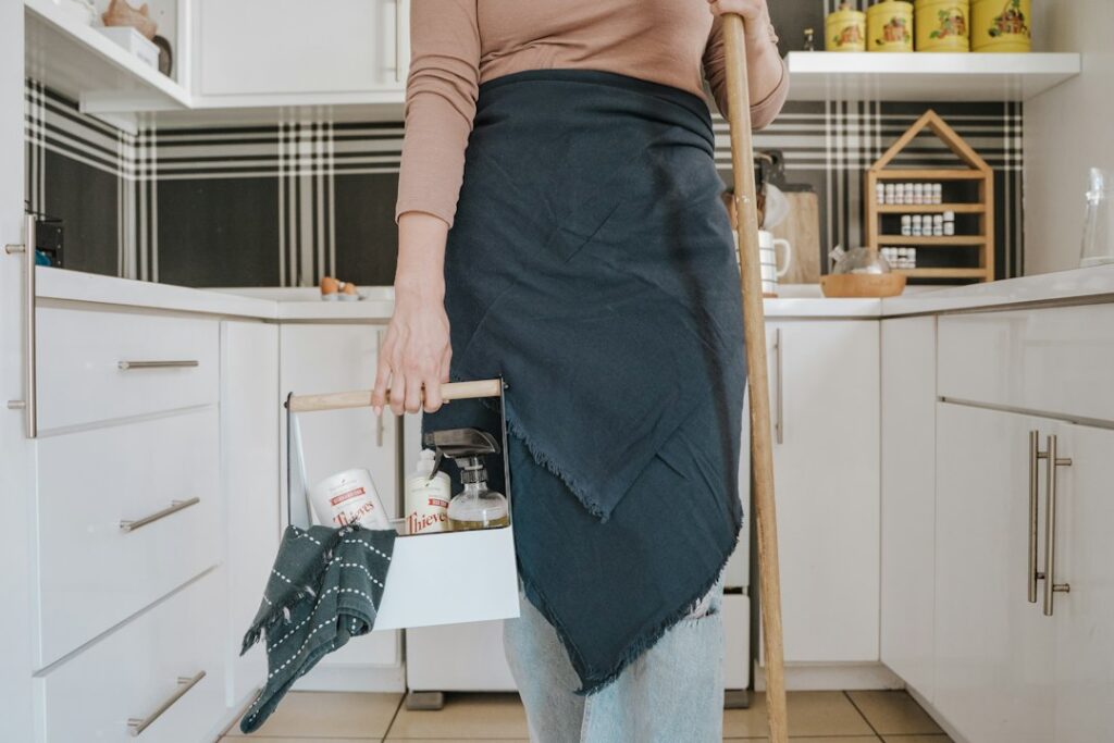 Adult lifting a laundry basket close to the body while bending through the knees in a bright home.